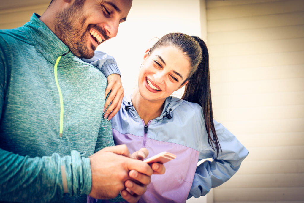 un homme et une femme en tenue de sport regardent un téléphone en souriant